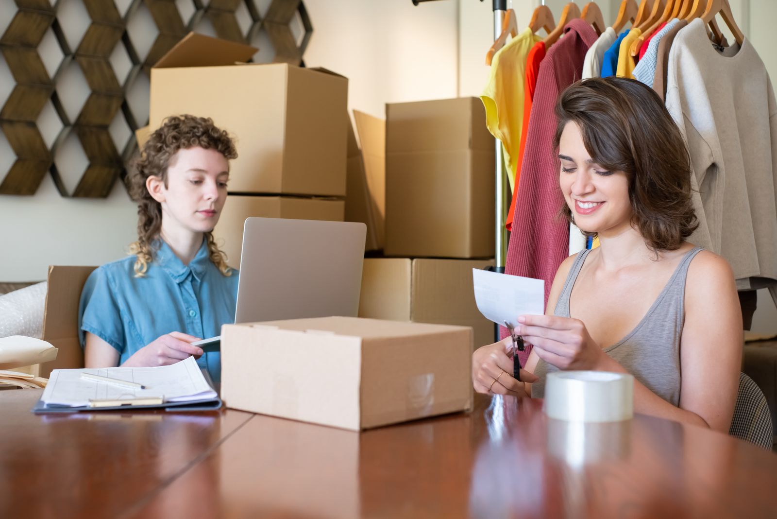 Two online sellers packing orders at a desk stacked with boxes